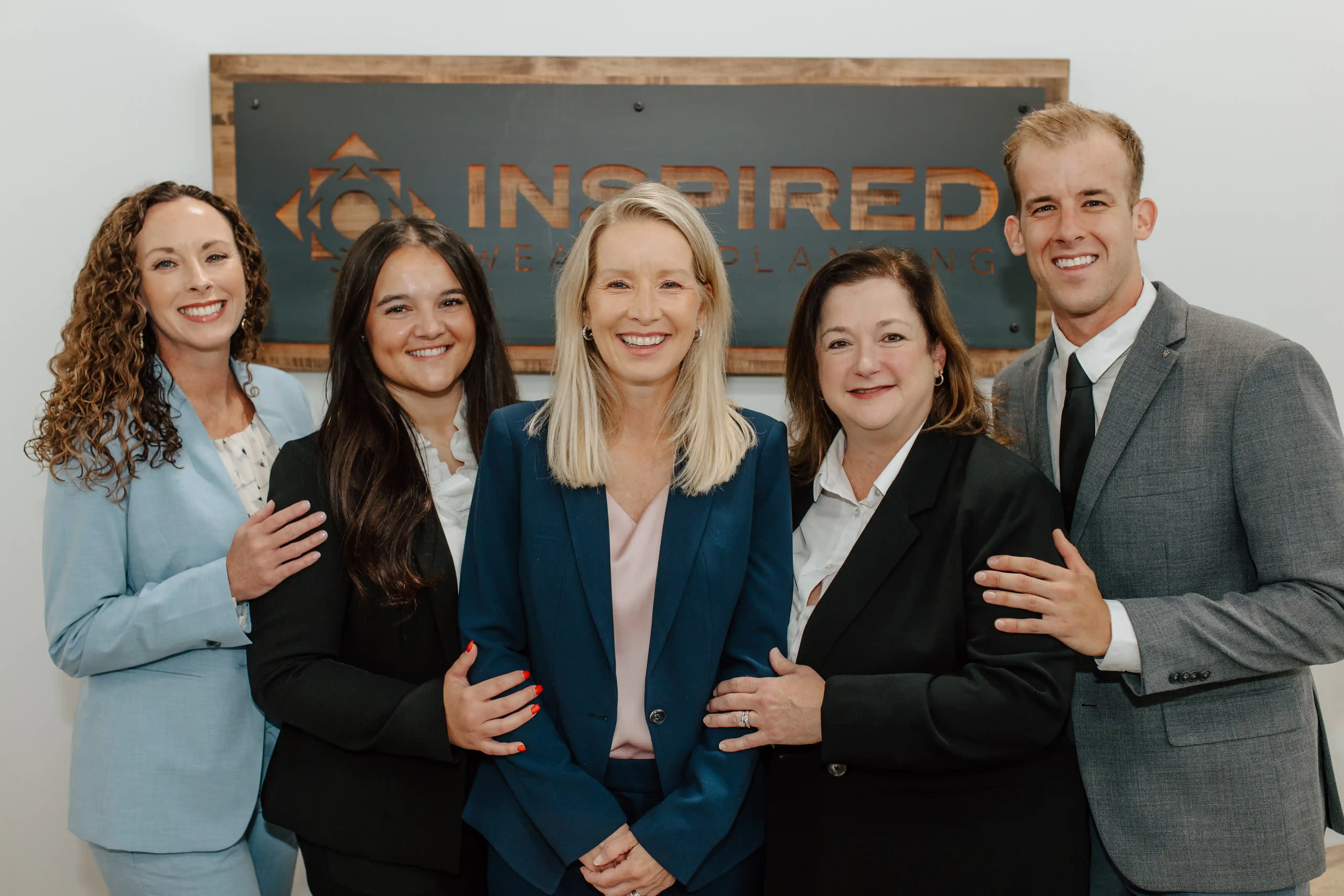 Griffin team of four women and a man standing close together in front of the Inspired sign